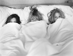 two women laying in bed with white sheets