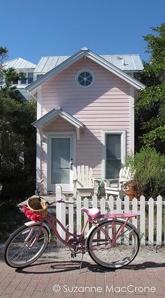 two bikes are parked in front of a pink house with white picket fence and trees