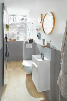 a white toilet sitting next to a bathroom sink under a round mirror on the wall