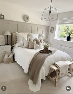 a white bed sitting in a bedroom next to a lamp and window with pictures on the wall