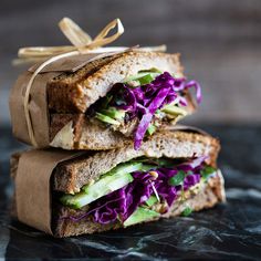 two sandwiches stacked on top of each other with purple cabbage and lettuce wrapped in brown paper