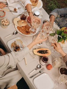 people are sitting at a table with food and drinks in front of them, all holding wine glasses