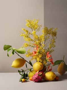 a vase filled with lots of yellow and pink flowers next to lemons on a table