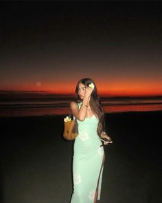 a woman in a green dress is holding a cell phone and standing on the beach