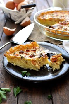 a piece of quiche on a black plate next to an egg in a bowl