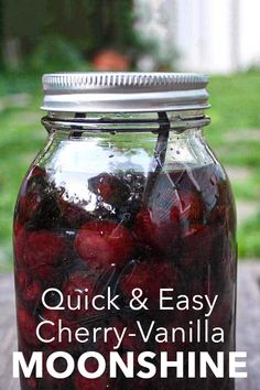 a mason jar filled with cherries sitting on top of a wooden table next to grass