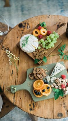 an assortment of cheeses, crackers and fruit on a wooden table next to a bottle of wine