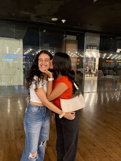 two women standing next to each other on a hard wood floored area with glass walls