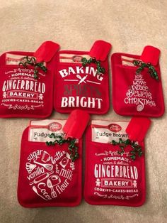 four red oven mitts sitting on top of a white table cloth covered in christmas decorations