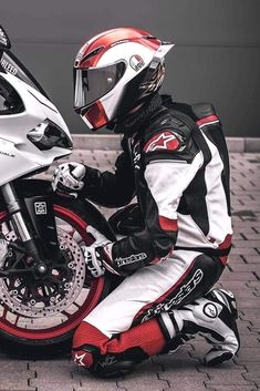 a man sitting on the ground next to a motorcycle wearing a red and white outfit