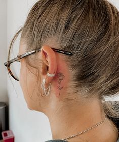 a woman wearing glasses has a small flower behind her ear and is looking at the wall