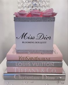 three books stacked on top of each other in front of a white wall with a pink rose