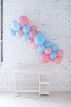 a bunch of balloons floating in the air next to a white table and brick wall