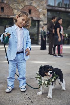 a little boy in a suit and tie holding a leash with a dog on a leash