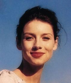 a close up of a person wearing a white shirt and smiling at the camera with a blue sky in the background