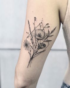 a black and white flower tattoo on the left upper half of the arm, with daisies growing out of it