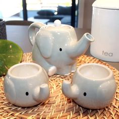 three ceramic elephants sitting on top of a wicker table next to a tea pot