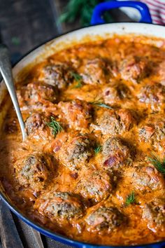 a blue pot filled with meatballs covered in sauce and garnished with fresh herbs