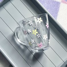 a glass cup with flowers painted on the inside sits on a wooden table next to a tray