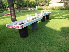 two benches sitting in the middle of a field with cups on them and one bench is empty