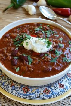 a bowl of chili with sour cream in it on a plate next to some peppers