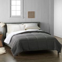 a bed with white pillows and gray comforter in a bedroom next to a window