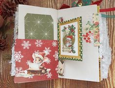 an open christmas card book sitting on top of a wooden table next to pine cones