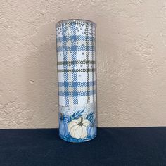 a blue and white plaid vase sitting on top of a black table next to a wall