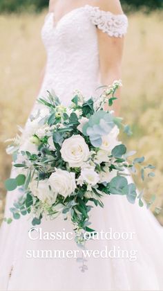 a bridal holding a bouquet of white flowers and greenery in front of a field