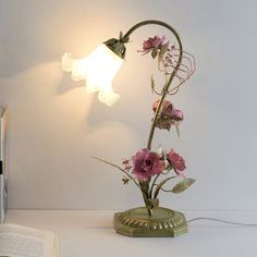 a lamp that is sitting on top of a table next to a book and some flowers