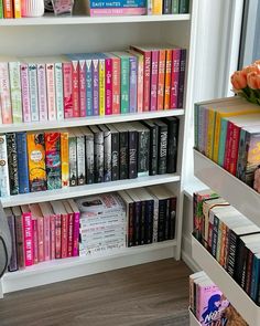 a book shelf filled with lots of books next to a vase full of flowers on top of a window sill