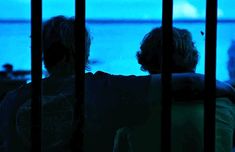 two people standing behind bars looking out at the ocean