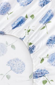 blue hydrangeas on white bedding with green leaves and flowers in the middle