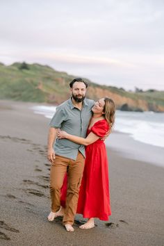 a man and woman standing on the beach with their arms around each other as they hug