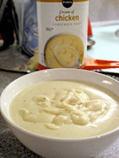 a white bowl filled with soup next to a can of chicken