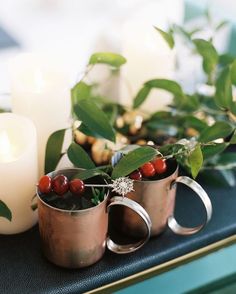 two mugs filled with cherries sit on a table next to candles and greenery