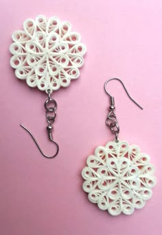 two pairs of white earrings are on a pink surface and one pair is made out of plastic