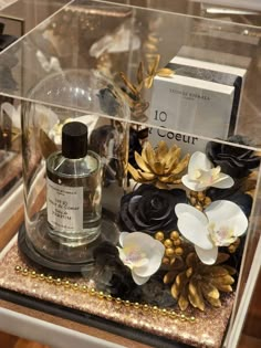 an assortment of perfumes and flowers on display in a glass case with gold sequins