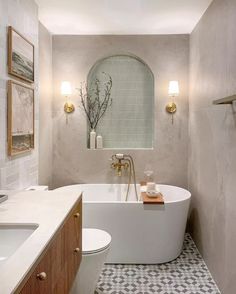 a white bath tub sitting next to a toilet in a bathroom under a window with gold fixtures