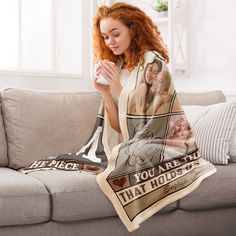 a woman sitting on a couch with a blanket over her face and holding a coffee cup