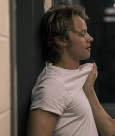 a person leaning against a wall with their hand on his chin and looking off into the distance