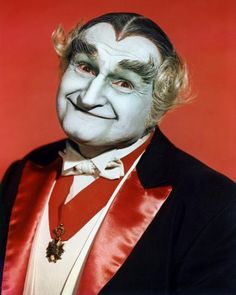 a man in a costume with white paint on his face and hair, wearing a red tie