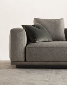 a gray couch with two pillows on it and a white wall in the back ground