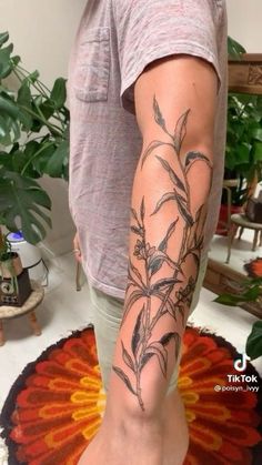 a man with a tattoo on his arm and leg is standing in front of a potted plant