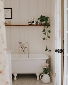 a white bath tub sitting under a window next to a plant in a vase on the floor