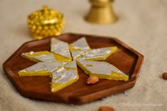 pieces of yellow and white cake sitting on a wooden plate with almonds around it