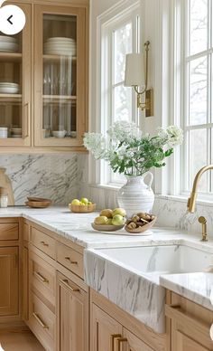 a kitchen with marble counter tops and wooden cabinets, along with white flowers in a vase