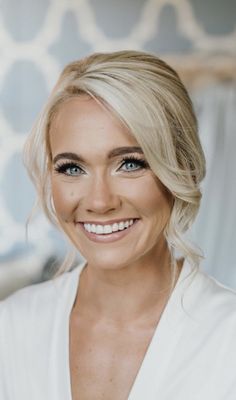 a woman with blonde hair and blue eyes smiles at the camera while wearing a white top