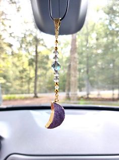 the inside of a car with a necklace hanging from it's dash board, in front of trees