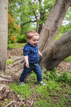 a young boy is walking through the grass in front of some trees and bushes with his mouth open